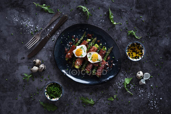 Dall'alto asparagi saporiti con uova di quaglia fritte ed erbe messe su boccia vicino a argenteria su cima di tavolo di marmo — Foto stock