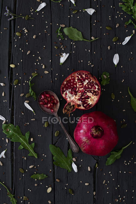 Top view of fresh pomegranates placed on plates near arugula and knife on lumber table — Stock Photo