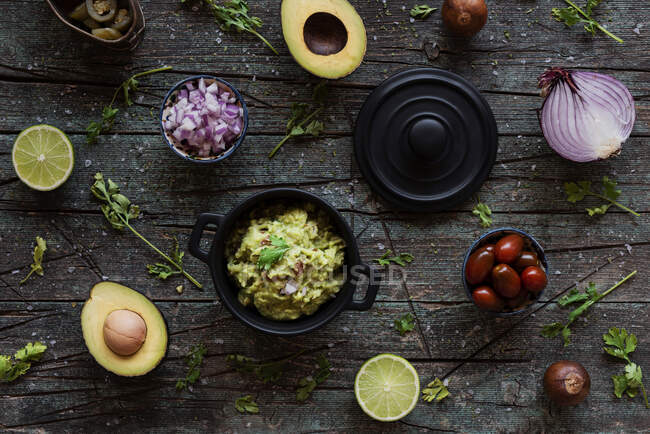 Vue de dessus de divers ingrédients frais placés sur la table de bois près de pot avec guacamole délicieux — Photo de stock