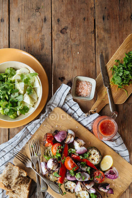 From above of aromatic delicious grilled vegetables including red tomatoes and pepper with sliced eggplants and onion served on wooden board on rustic table with homemade dishes — Stock Photo