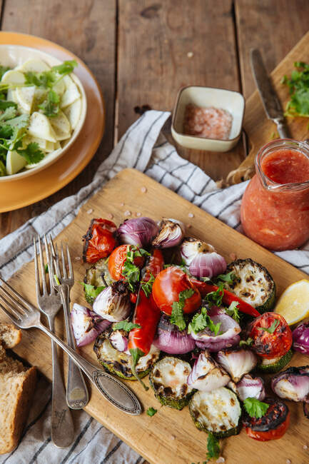 Von oben von aromatischen köstlichen gegrillten Gemüse einschließlich roter Tomaten und Paprika mit geschnittenen Auberginen und Zwiebeln serviert auf Holzbrett auf rustikalem Tisch mit hausgemachten Gerichten — Stockfoto