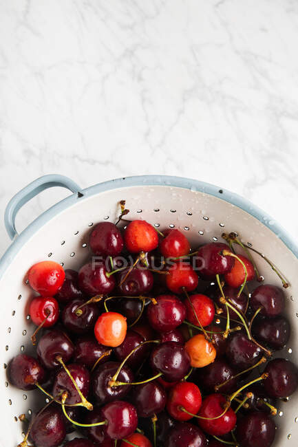Top view of colander with clean wet cherry placed on marble table in kitchen — Stock Photo