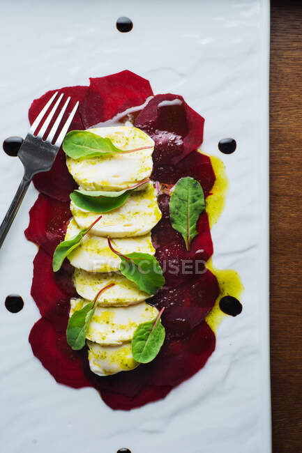 Зверху елегантний ресторанний салат, зроблений з сиром моцарели та буряком, прикрашений свіжим шпинатом та соусом, який подається на білому підносі з виделкою — стокове фото