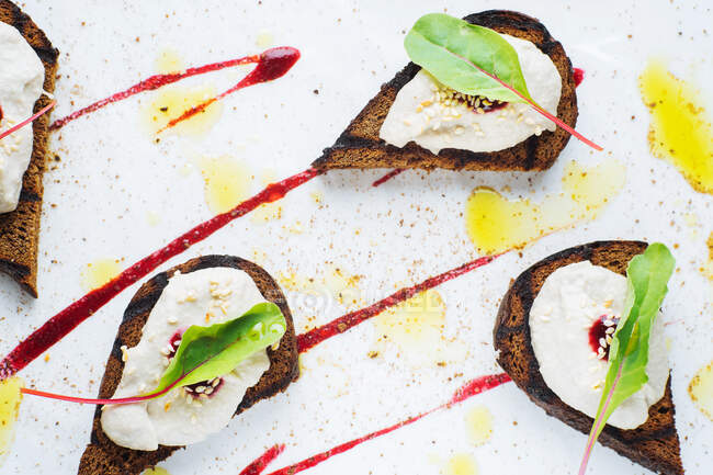From above of delicious grilled toasts with ricotta cheese and fresh beetroot leaves garnished with sauce served on white plate in luxury restaurant — Stock Photo
