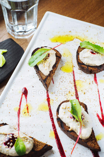 Сверху вкусные тосты на гриле с рикоттой и свежими свекловичными листьями, украшенными соусом, подаваемые на белой тарелке в роскошном ресторане — стоковое фото