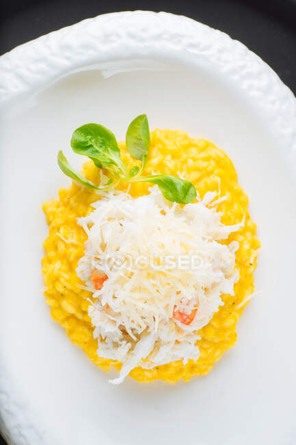 Von oben das traditionelle Safranrisotto mit Parmesan, garniert mit grünen Kräutern, serviert auf einem weißen Teller auf einem Holztisch mit einem Glas Weißwein — Stockfoto