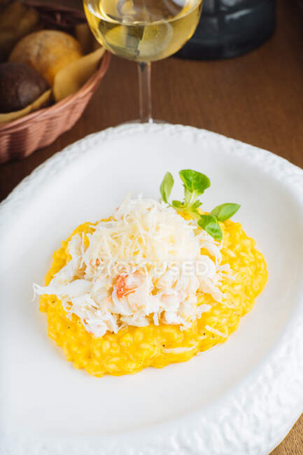 From above of traditional saffron risotto with Parmesan cheese garnished with green herbs served on white plate on wooden table with glass of white wine — Stock Photo