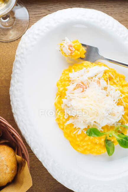From above of traditional saffron risotto with Parmesan cheese garnished with green herbs served on white plate on wooden table with glass of white wine — Stock Photo