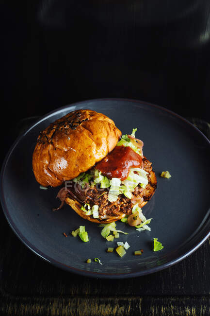 De cima de delicioso hambúrguer gourmet com ervas verdes picadas e molho de tomate servido em placa de cerâmica preta no fundo preto — Fotografia de Stock