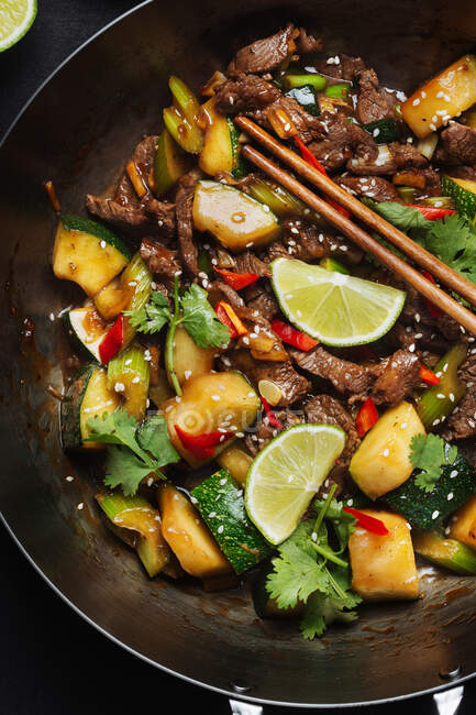 Dall'alto del wok piccante asiatico mescolare il piatto fritto con carne e zucchine guarnite con lime fresco e coriandolo. — Foto stock