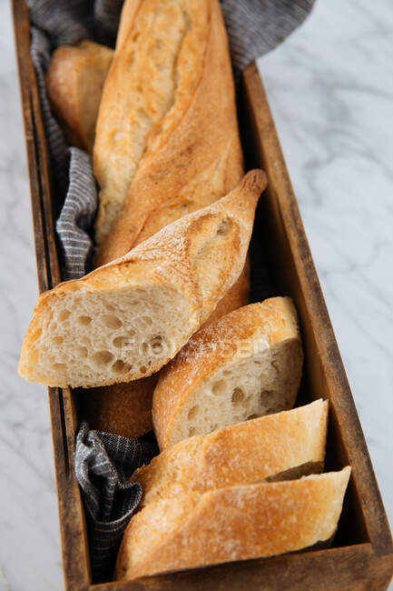 Draufsicht auf köstliches frisches Baguette in Scheiben, serviert auf Holztablett auf Marmortisch — Stockfoto