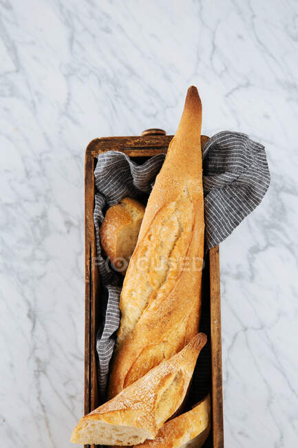 Top view of delicious fresh sliced baguette served on wooden tray placed on marble table — Stock Photo