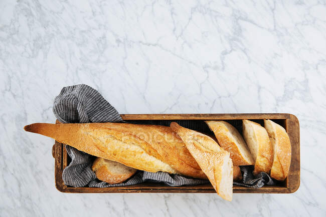 Vista superior da deliciosa baguete fatiada fresca servida em bandeja de madeira colocada na mesa de mármore — Fotografia de Stock
