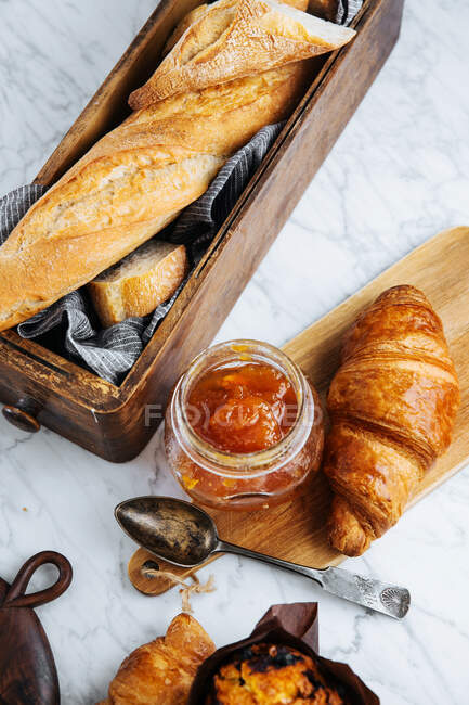 Zusammensetzung von frischem Baguette und Croissants mit aromatischer süßer Marillenmarmelade auf Marmortisch — Stockfoto