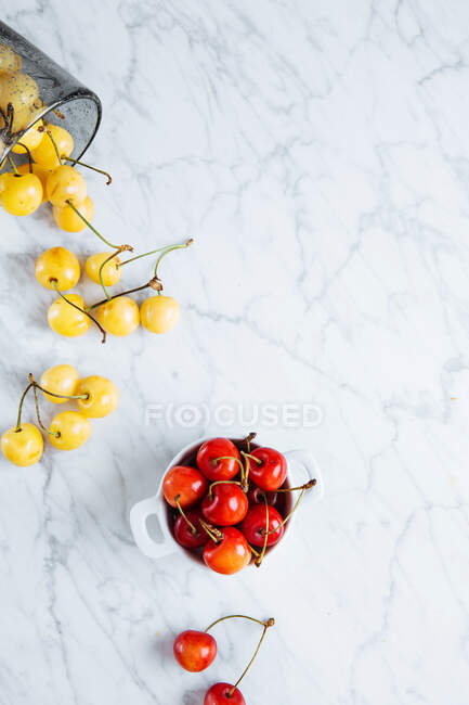 Vue du dessus du pot avec des cerises jaunes rouges mûres fraîches placées près du verre tombé avec des cerises jaunes sur la table en marbre — Photo de stock