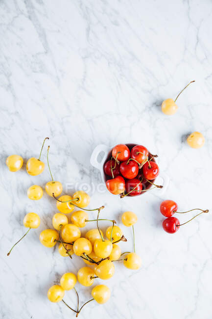 Top view of pot with fresh ripe red yellow cherries placed near fallen glass with yellow cherries on marble table — Stock Photo
