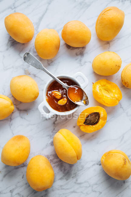 Draufsicht auf weißen Teller mit frischen gelben reifen Aprikosen auf weißem Marmortisch mit halbierter Aprikose und Marmelade im Glas — Stockfoto