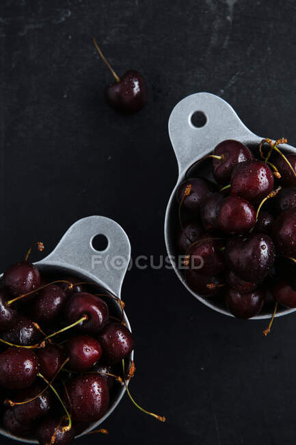 Top view of pots with ripe sweet red cherries on dark marble table with green branch — Stock Photo