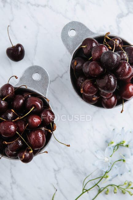 Draufsicht auf Töpfe mit reifen süßen roten Kirschen auf dem Marmortisch mit grünem Zweig — Stockfoto