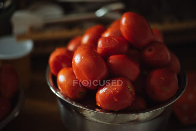 Зверху свіжі стиглі червоні виноградні помідори з краплями води в металевій мисці, розміщеній на дерев'яному столі на кухні — стокове фото