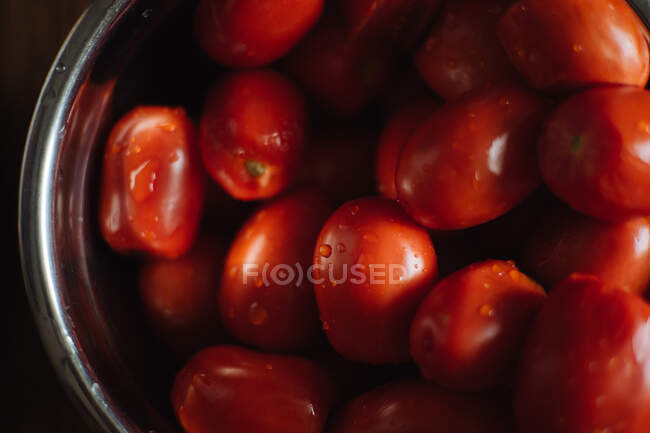 From above of fresh ripe red grape tomatoes with water drops in metal bowl placed on wooden table in kitchen — Stock Photo