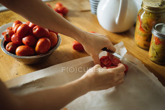 Lavoura dona de casa colocando cortar tomates frescos na assadeira enquanto prepara conservas caseiras tradicionais na mesa de madeira na cozinha — Fotografia de Stock