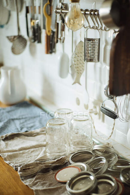 Vasi di vetro lavato e coperchi di metallo preparati per l'inscatolamento e la conservazione posti sul tavolo in cucina domestica con utensili — Foto stock