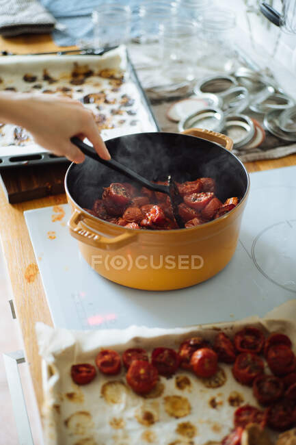 Растениеводство неузнаваемая домохозяйка с лопаткой держа горячую сковороду с вареными помидорами при подготовке вкусный соус на кухне — стоковое фото