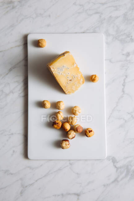 Вид зверху смачний гастрономічний блакитний сир і лісові горіхи, подані на білій дошці на мармуровому столі — стокове фото