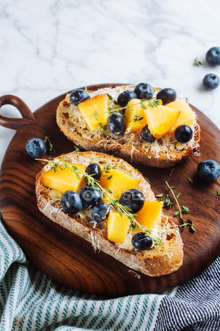Top view of appetizing healthy sandwiches made with homemade bread and fresh apricot and blueberries garnished with thyme on wooden board on white marble table — Stock Photo