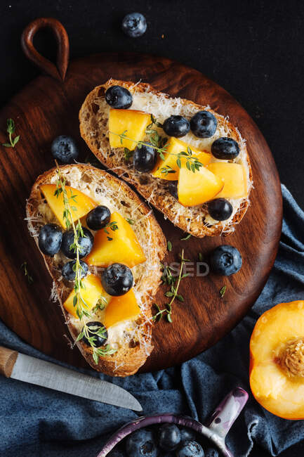 Draufsicht auf appetitliche gesunde Sandwiches mit hausgemachtem Brot und frischen Aprikosen und Blaubeeren garniert mit Thymian auf Holzbrett auf dunklem Marmortisch — Stockfoto