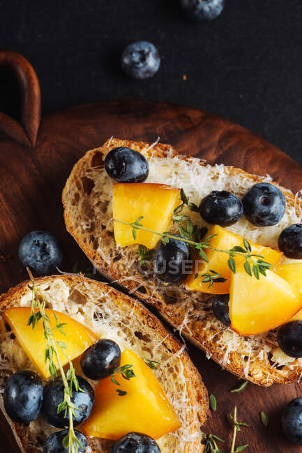 Top view of appetizing healthy sandwiches made with homemade bread and fresh apricot and blueberries garnished with thyme on wooden board on dark marble table — Stock Photo