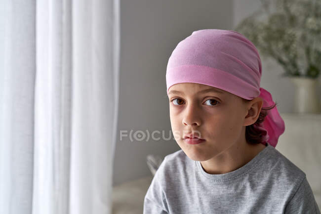 Серйозна мила дитина в рожевому бандані дивиться на камеру і бореться з раком вдома. — стокове фото
