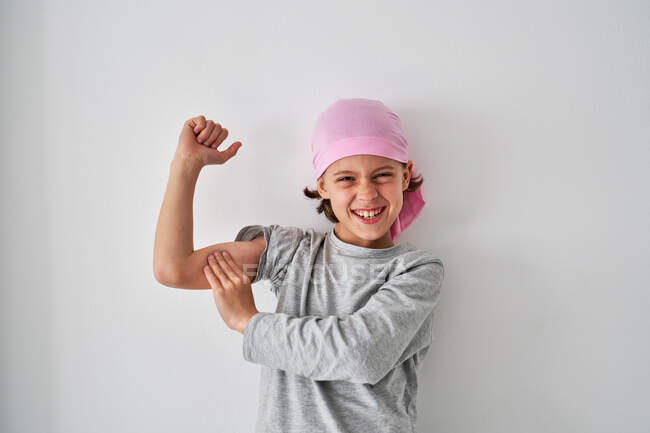 Відважна дитина з діагнозом раку дивиться на камеру і верещить, коли піднімає кулаки на сірому фоні. — стокове фото