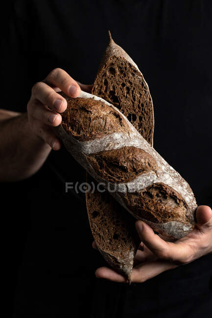 Cultivo panadero masculino en delantal sosteniendo cortado en media hogaza de pan fresco y saludable artesanal - foto de stock