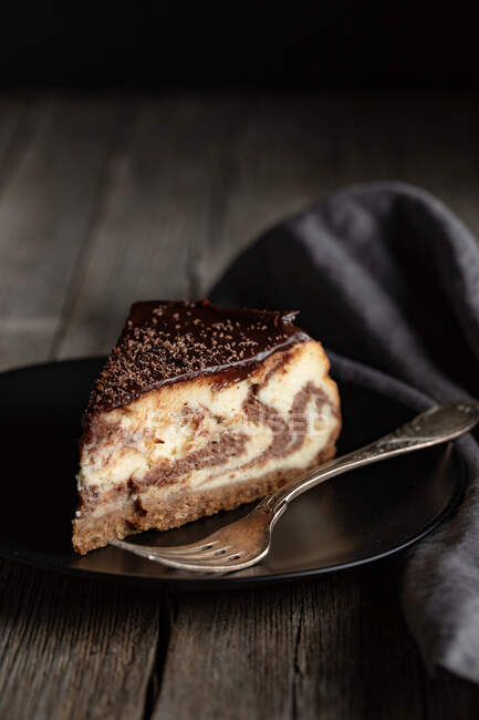 Pedaço de delicioso bolo caseiro de mármore ou zebra com cobertura de chocolate servido em placa preta com garfo na mesa de madeira escura — Fotografia de Stock