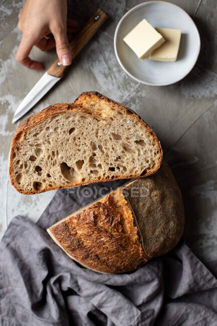De arriba de la cosecha cuchillo hembra con la mitad cortada de deliciosa masa fermentada pan pan sobre mesa de madera con cuchillo y mantequilla - foto de stock