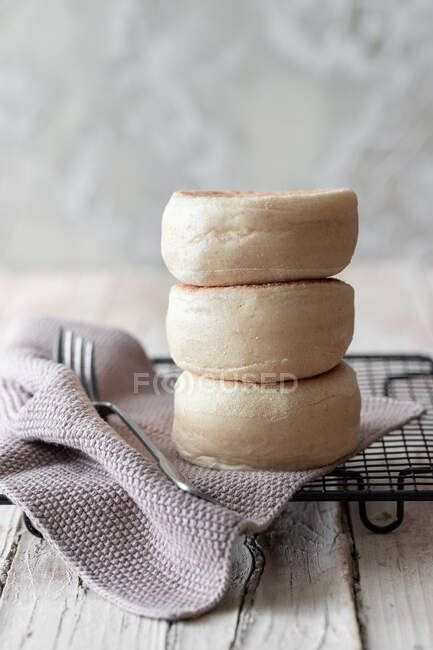 Tasty fresh homemade buns stacked on metal grid with gray cloth and fork on wooden table — Stock Photo