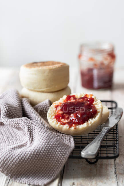 Appetizing freshly baked bun cut in half with homemade strawberry jam placed on metal grid with gray cloth and knife on kitchen table — Stock Photo