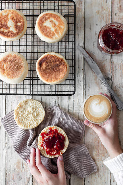 From above of crop female having breakfast at wooden table with cup of cappuccino and fresh homemade buns with berry jam — Stock Photo