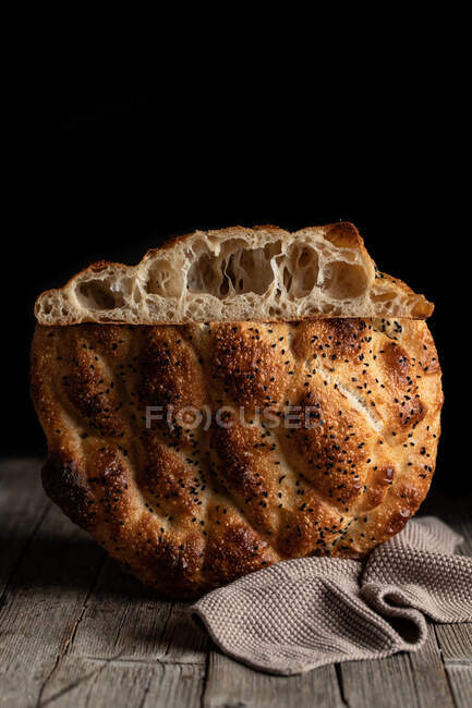Fresh appetizing braided round bread with seeds placed on wooden table with napkin on black background — Stock Photo
