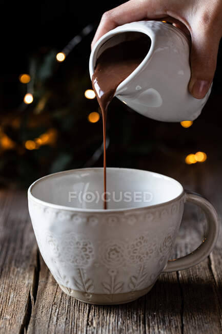 Crop woman pouring delicious hot chocolate into elegant white cup placed on wooden table — Stock Photo