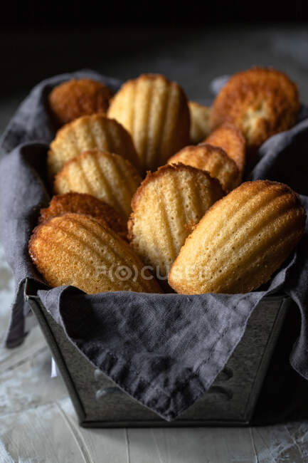 Traditional yummy homemade Madeleine cookies placed on black container with napkin on wooden table — Stock Photo