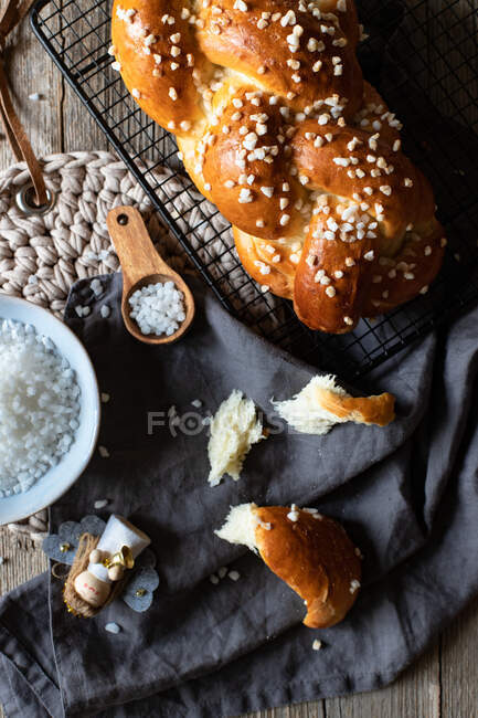 Top view of fresh appetizing braided round bread with sprinkles placed on metal grid on table with Christmas decorative elements — Stock Photo