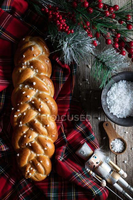 Vue du dessus de la table en bois avec du pain tressé traditionnel coupé et un couteau posé sur une nappe de Noël à carreaux avec des objets décoratifs — Photo de stock
