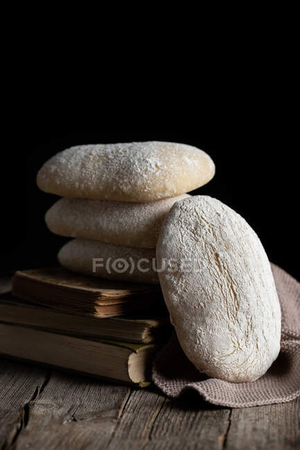 Haufen frisch gebackenes leckeres hausgemachtes Brot auf Holztisch neben geschnittenem Stück vor schwarzem Hintergrund — Stockfoto
