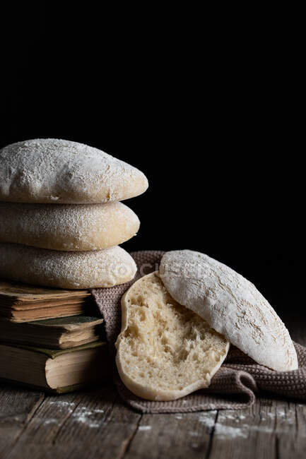 Pile of freshly baked tasty homemade bread placed on wooden table next to cut piece against black background — Stock Photo