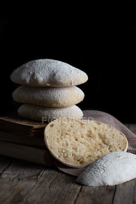 Pile of freshly baked tasty homemade bread placed on wooden table next to cut piece against black background — Stock Photo