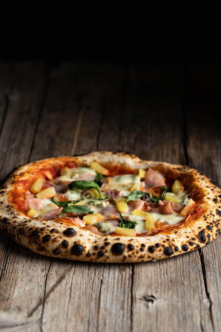 Von oben hausgemachte Pizza mit Schinken, Ananas, Basilikumblättern und Tomaten mit Käse auf Holzboden — Stockfoto