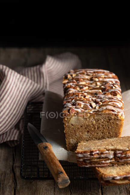 From above sliced appetizing homemade banana bread with nuts and sugar icing placed on wooden table with knife and tablecloth — Stock Photo